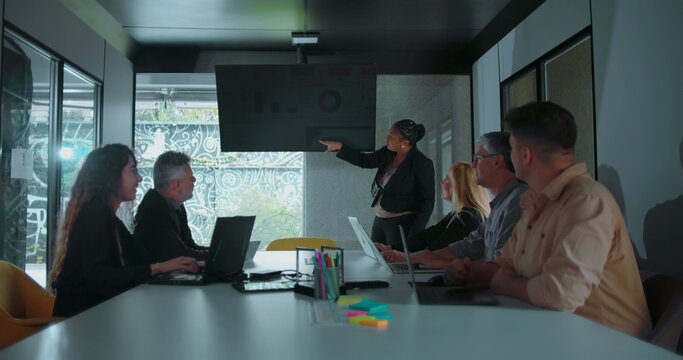African American businesswoman explaining data during team presentation as colleagues look on in well lit modern conference room