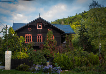 A large dark timber villa with ornate trim and blue roof sits among dense greenery and colorful...