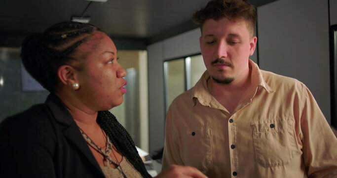 African American businesswoman explaining tablet data to young male colleague in office, active teamwork near conference table with charts on screen
