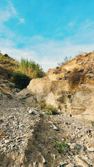 Rocky dry river gorge with different species of vegetation under blue sky with some clouds. Malaga, Andalusia, Spain.