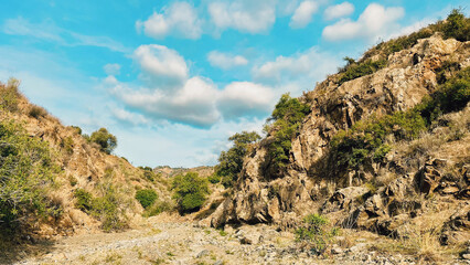 Rocky dry river gorge with different species of vegetation under blue sky with some clouds. Malaga, Andalusia, Spain.