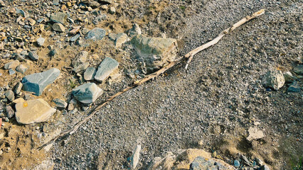 Piece of dead wood lying on pebble stones in dry river bed. Top view.