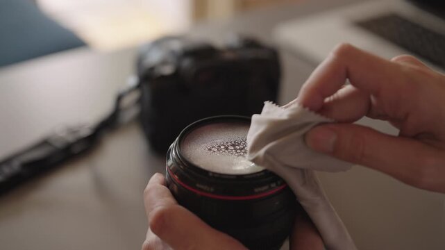 Closeup of photographer maintaining professional equipment by spraying cleaning fluid and wiping camera lens with soft microfiber cloth in meticulous process for clear optics. Shooting in slow motion.