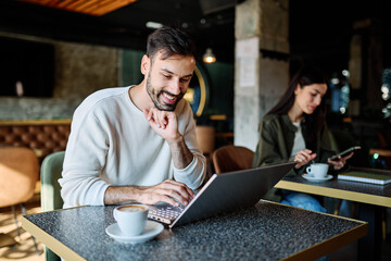 Man and woman smiling, holding coffee while working on a laptop and using a mobile phone  in a cafe