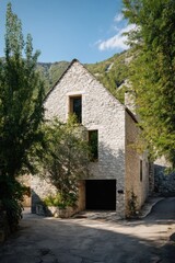 Fototapeta premium Nestled in a serene mountain village, a stunning stone house stands gracefully amidst vibrant greenery, basking in the warmth of a sunny day