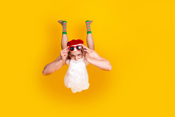 Santa on a bright yellow background upside down wearing hat beard striped socks and sunglasses for...