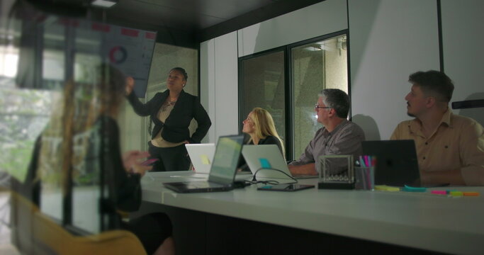 African American businesswoman presenting in office meeting while diverse team listens attentively in modern conference room with digital chart display