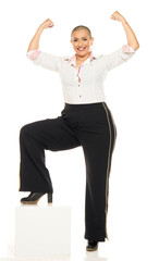 Studio shot of bald woman in patterned shirt and black pants flexing both arms and smiling on white background, full length.