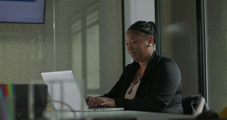 African American businesswoman smiling softly while typing on laptop during quiet work moment in modern office setting