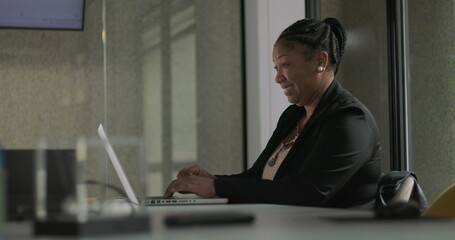 African American businesswoman smiling with fist raised in excitement while working on laptop in office meeting room