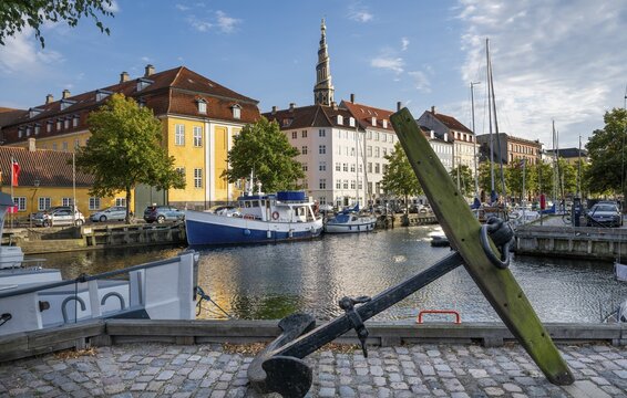 Old anchor, sailing boats, historic buildings and tower of Vor Frelsers Kirke or Church of the Saviour, Christianshavn Canal, Copenhagen, Denmark