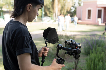 Primer plano de joven con cámara en mano y monitor digital filmando secuencia al aire libre