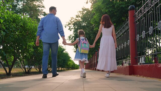 Child daughter, dad mom walk down street holding hands, family walk. Father mother take their child to school outside. Happy family, park. Kid girl parents walk to school. Children education concept