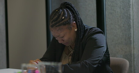 African American corporate employee leans forward at table with face hidden behind hands, conveying...