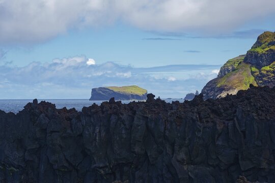 View of a rocky coastline with a small island in the background under a cloudy sky by the sea, Termas da Ferraria, Sao Miguel Island, Azores, Portugal