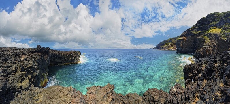 Panoramic view of a rocky lava coast with clear blue water and clouds in the sky, Termas da Ferraria, Sao Miguel Island, Azores, Portugal