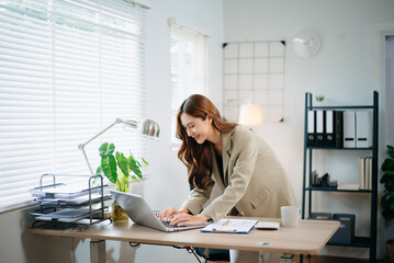Confident business expert attractive smiling young woman typing laptop and holding digital tablet in green office