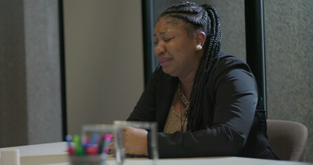 African American corporate employee leans forward at table with face hidden behind hands, conveying...