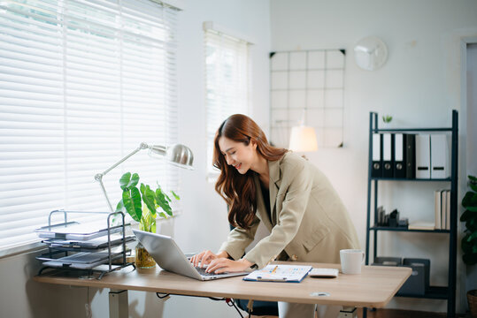 Confident business expert attractive smiling young woman typing laptop and holding digital tablet in green office
