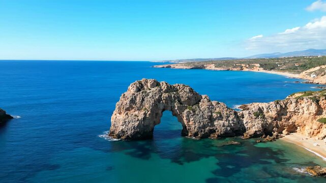 Aerial view of a stunning arch rock formation in the sea under blue sky. Azure waters and sandy beaches compose a beautiful landscape