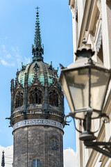 Sharp view of the Castle Church tower in Wittenberg, Germany, with a blurred historic street lantern in the foreground. Iconic Reformation site linked to Martin Luther.