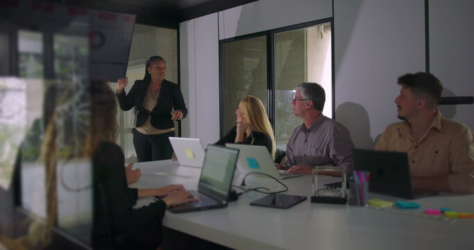 African American professional presenting during team meeting while colleagues observe digital screen in well lit corporate boardroom