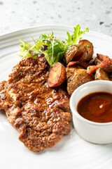 A perfectly pan-fried pork schnitzel is served with crispy roasted baby potatoes, a fresh green salad, and a side of savory red sauce on a white plate