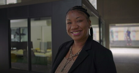 African American woman smiling warmly standing near glass office wall conveying friendliness confidence and approachability in professional workplace setting