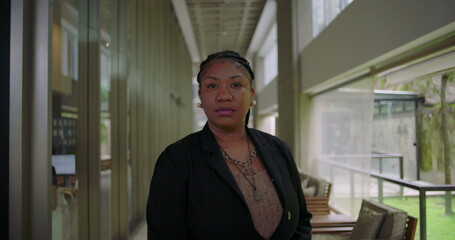 African American woman standing confidently in modern office hallway looking serious and focused professional corporate portrait leadership presence workplace diversity