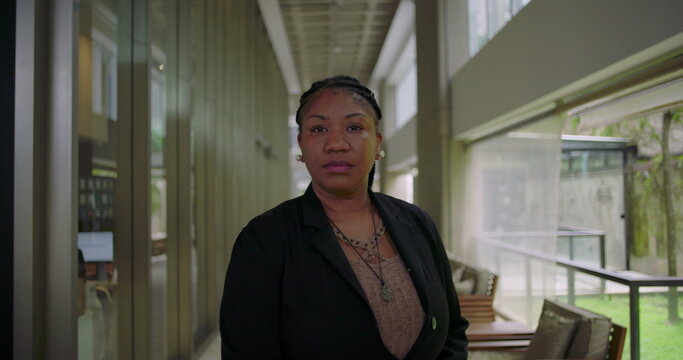 African American woman standing confidently in modern office hallway looking serious and focused professional corporate portrait leadership presence workplace diversity