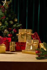 A vertical composition with gold and red Christmas gifts on a wooden table next to a tree. The scene perfect for seasonal greeting cards or product mockups.