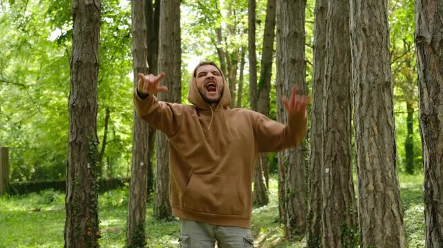 A man jumps energetically on a forest path, raising his hands in a rock gesture with an open-mouth expression of excitement. Concept highlights joy, freedom, energy and bold self-expression