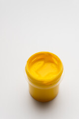 A jar of yellow colored gouache on a white background. Copy space. A transparent jar of colored water-soluble paint.