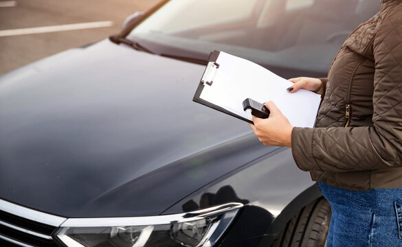 Female Stands By Automobile With Alcohol Tester And Clipboard. Preparing To Document Sobriety Check Results.