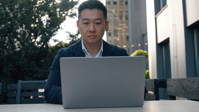 Focused Asian business man with laptop computer Korean businessman working corporate network productivity project expertise job Chinese Japanese middle-aged male entrepreneur in city expert agent - Powered by Adobe