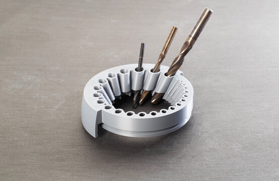 A gray round tool with holes of different sizes for sharpening drills through a grinder, close-up, gray background. Metal drills - Powered by Adobe