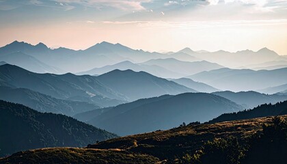 A panoramic view of multiple mountain ranges receding into the distance under a soft, hazy sky.