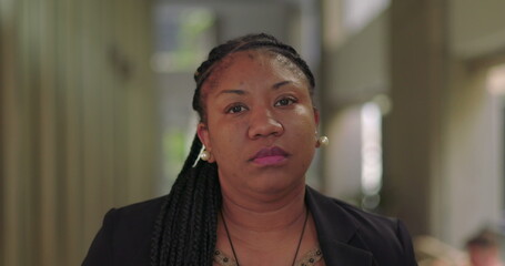 African American woman with braids looking serious and composed in modern office hallway with vertical panels and natural light in background
