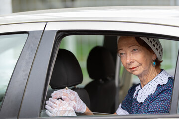 Older woman with lace gloves sitting in car during day, looking thoughtfully outside the window