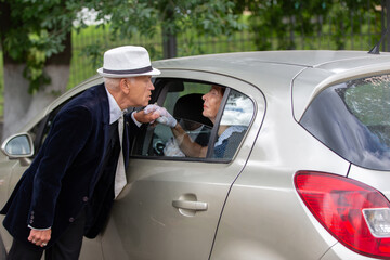 Elderly couple shares a heartfelt moment by a parked car during a sunny afternoon
