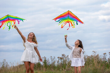 Two girls flying colorful kites in an open field on a cloudy day with soft grasses surrounding them