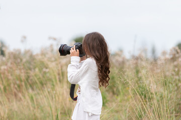 Young girl capturing nature with a camera in a grassy field during a cloudy day