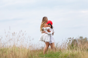 Mother and child enjoying a playful moment outdoors with a red balloon in a grassy field on a cloudy day