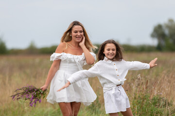 Mother and daughter joyfully playing in a field on a cloudy day with wildflowers