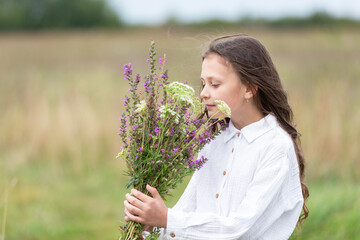 Girl enjoys nature while holding a bouquet of wildflowers in a grassy field during a sunny afternoon