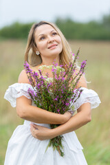 Woman holds a bouquet of wildflowers in a field during a cloudy day
