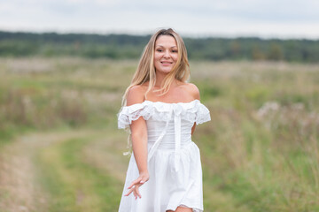 Young woman walks through a grassy field wearing a white dress, enjoying a quiet day outdoors in nature