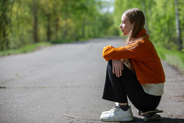 Young girl with long hair sitting on a skateboard in a peaceful park environment under natural light