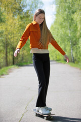 Young girl skateboarding on a sunny day in a green park surrounded by trees