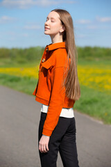 Young woman enjoys sunny day outdoors while wearing stylish orange jacket and black pants